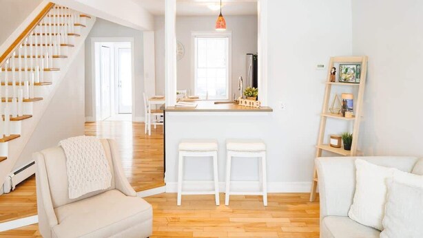 A modern kitchen with white bar stools, a wooden staircase, and a white sofa. - 67 - Walking distance to downtown (Charlottetown)