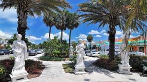 A statue-lined pathway with palm trees and a clear blue sky.