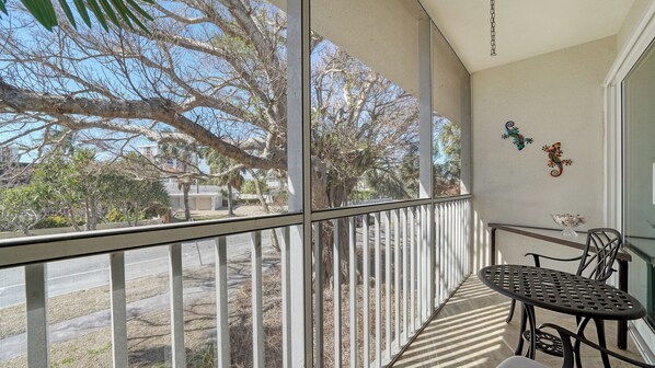 A balcony with a metal table and chairs, a white railing, and decorative wall art.