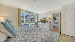 A bedroom with a large bed, a dresser, a television, and a view of the outdoors.