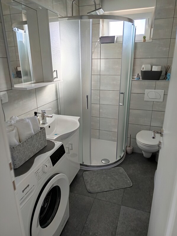 A modern bathroom with a glass-enclosed shower, a built-in washing machine, a sink, and a toilet.