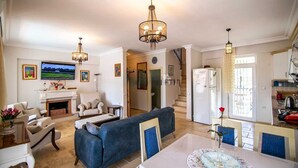 Ein geräumiges Wohnzimmer mit Kamin, einem blauen Sofa, einem Esstisch mit Stühlen und einer Küchenzeile mit Kühlschrank und Herd.