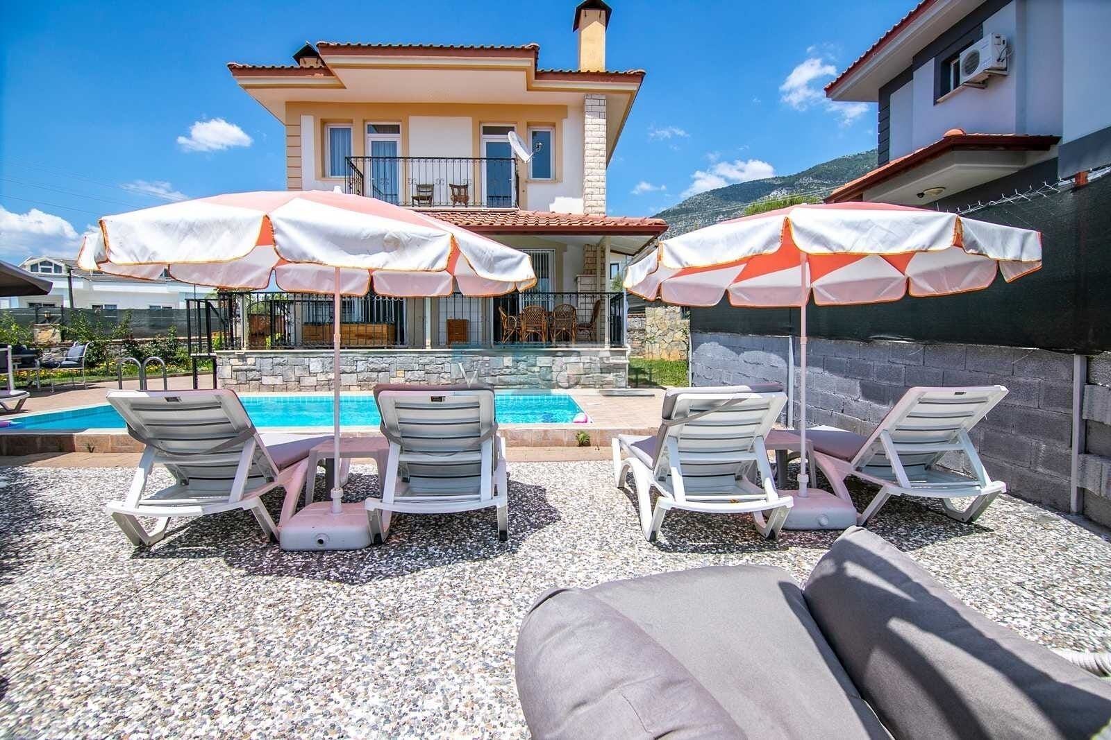 A poolside area with lounge chairs and umbrellas, a pool, and a building in the background.