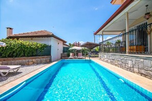 A swimming pool with lounge chairs and umbrellas, surrounded by stone walls and a covered patio area. - Villa Palm (Fethiye)
