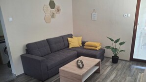 Un salon moderne avec un canapé d’angle gris, une table basse en bois et une plante en pot.