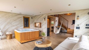 A modern living room with a wooden floor, a large sofa, a round wooden coffee table, a hot tub, and a staircase leading to a dining area.