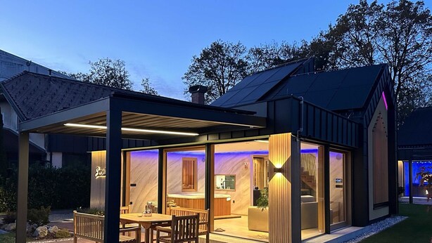 A modern house with a covered patio, a dining area, and a kitchen visible through glass doors.