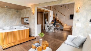 Ein modernes Wohnzimmer mit Holzboden, einer großen Couch, einem Holztisch, einem Hängekorbstuhl, einer Treppe und einem Whirlpool.