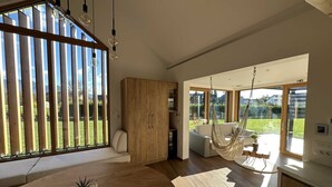 Ein geräumiges Wohnzimmer mit großem Fenster, einem Holzschrank, einem Hängekorbstuhl und einem Blumentopf.