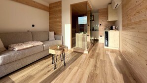 Una sala de estar moderna con un sofá, una pequeña mesa de madera y una cocina con armarios de madera y horno empotrado.