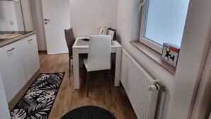 A compact room with a kitchenette, a dining table with a chair, a radiator, and a window with a view. - Charming Rustic Apartments Brest - One Bedroom Apartment (Ig)