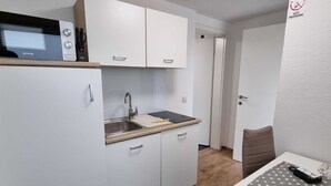 A compact kitchen with white cabinets, a sink, and a microwave. There is a dining area with a table and chairs. - Charming Rustic Apartments Brest - One Bedroom Apartment (Ig)