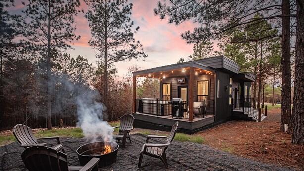 Una cabaña con terraza, un brasero y asientos al aire libre.