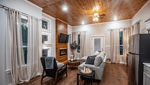 Una sala de estar acogedora con chimenea, un sofá, un sillón, un televisor montado en la pared y un refrigerador.