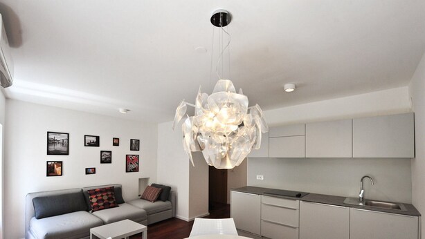 A modern living room with a grey sofa, a white dining table, and a kitchen area with grey cabinets and a stainless steel sink. - Downtown Piran Apartment with City View - Studio Apartment (Piran)