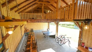 Une pièce rustique en bois, avec une longue table à manger et des chaises, une table de ping-pong et des vélos.