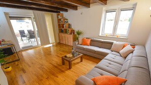 Un salon avec un plancher en bois, un canapé gris agrémenté de coussins orange, une table basse et une bibliothèque.
