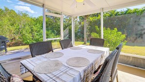 Eine überdachte Terrasse mit Tisch für vier Personen, umgeben von Korbstühlen, mit Blick auf einen üppigen Garten.
