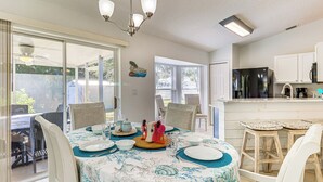 Ein Essbereich mit Tisch für vier Personen, eine Küche mit Kühlschrank und eine Glastür, die zu einer Terrassenförmigen Außenanlage führt.