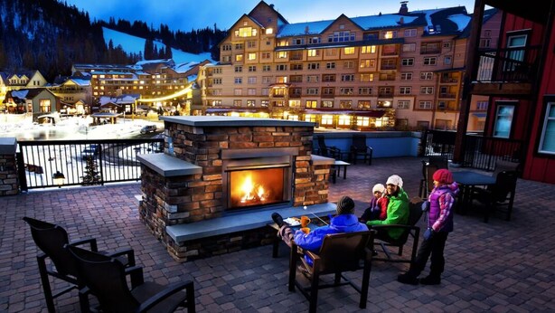 A stone fireplace with a fire, outdoor seating, and a view of a large building in the background.