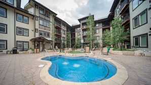 A swimming pool surrounded by a brick patio, with multi-story buildings in the background.