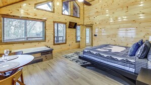 Ein Holzblockhaus-Interieur mit einem Bett, einem Esstisch und einer Badewanne.