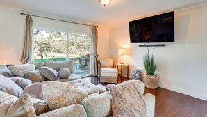 A living room with a large sofa set, a flat-screen TV mounted on the wall, a small side table with a lamp, and a potted plant. - Golfer's Oasis: Luxe Pebble Beach Home on 5th Hole (Pebble Beach)