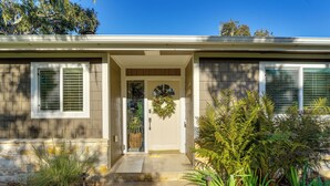 A two-story house with a front porch, a door with a wreath, and a small garden with various plants. - Golfer's Oasis: Luxe Pebble Beach Home on 5th Hole (Pebble Beach)
