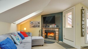 A cozy living room with a gray sectional sofa, a fireplace, and a television mounted on the wall. - Walk to Mount Snow Resort: Unit w/ Pool & Hot Tubs (Dover)