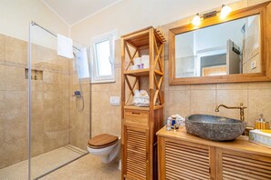Bathroom features a shelf, round sink, glass-enclosed shower, and separate toilet.