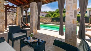 A covered outdoor seating area with stone pillars, wicker furniture, and a view of a swimming pool. - Villa Forte with Heated Private Pool close to the Beach (Porat (Krk))
