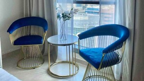 A modern hotel room with two blue chairs, a small table with a vase, and a large window offering a city view. - Cozy Studio Dubai Marina by beach & Metro (Dubai Marina)