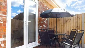 An outdoor patio with a table and chairs, a sliding glass door, and a wooden fence. - Rosedene Cottage - UK48604 (Chapel St. Leonards)
