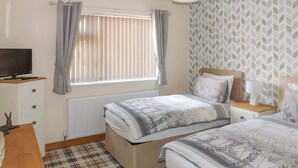 A bedroom with two beds, a dresser, a TV, and a window with curtains. - Rosedene Cottage - UK48604 (Chapel St. Leonards)