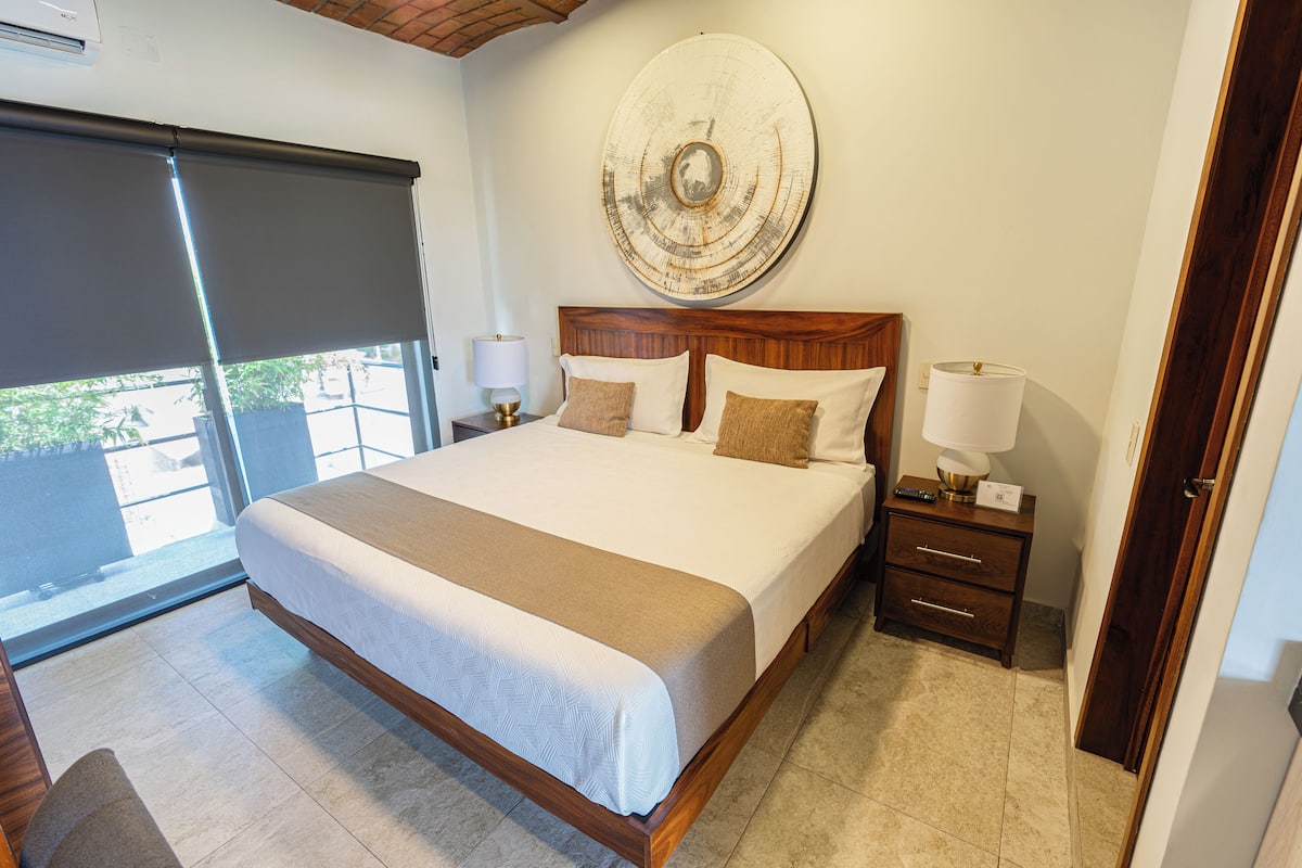 Um quarto espaçoso com uma cama grande, cabeceira de madeira e vista para o exterior por uma porta de correr.
