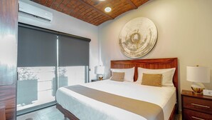 Ein Hotelzimmer mit einem großen Bett, einem Holzkopfende, einem an der Wand befestigten Kunstwerk, einem Nachttisch mit Lampe und einer Glastür zum Außenbereich.
