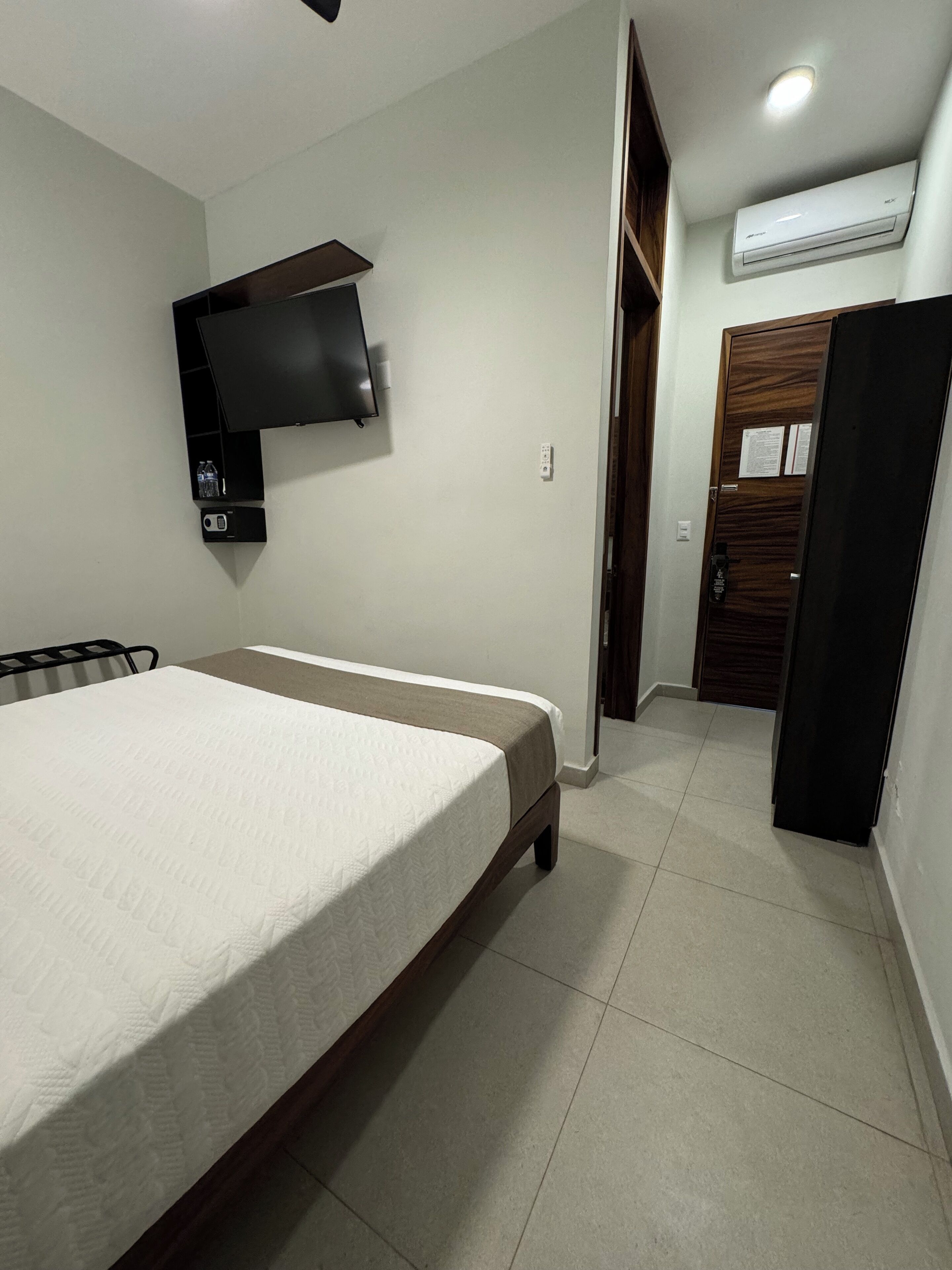 Une chambre à coucher comprenant un lit, un téléviseur fixé au mur, un climatiseur et une armoire.