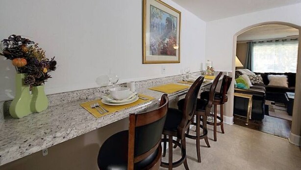 A dining area with a marble countertop, chairs, and a vase with dried flowers.