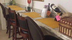 A dining area with a long table, multiple chairs, a framed picture on the wall, and a small plant.