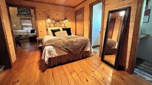 Acogedor dormitorio de cabaña de madera con cama, espejo y un pequeño rincón de descanso con sofá y mesa.