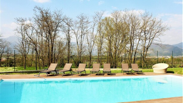 Una piscina con sillones de descanso y tumbonas, rodeada de árboles y montañas al fondo.