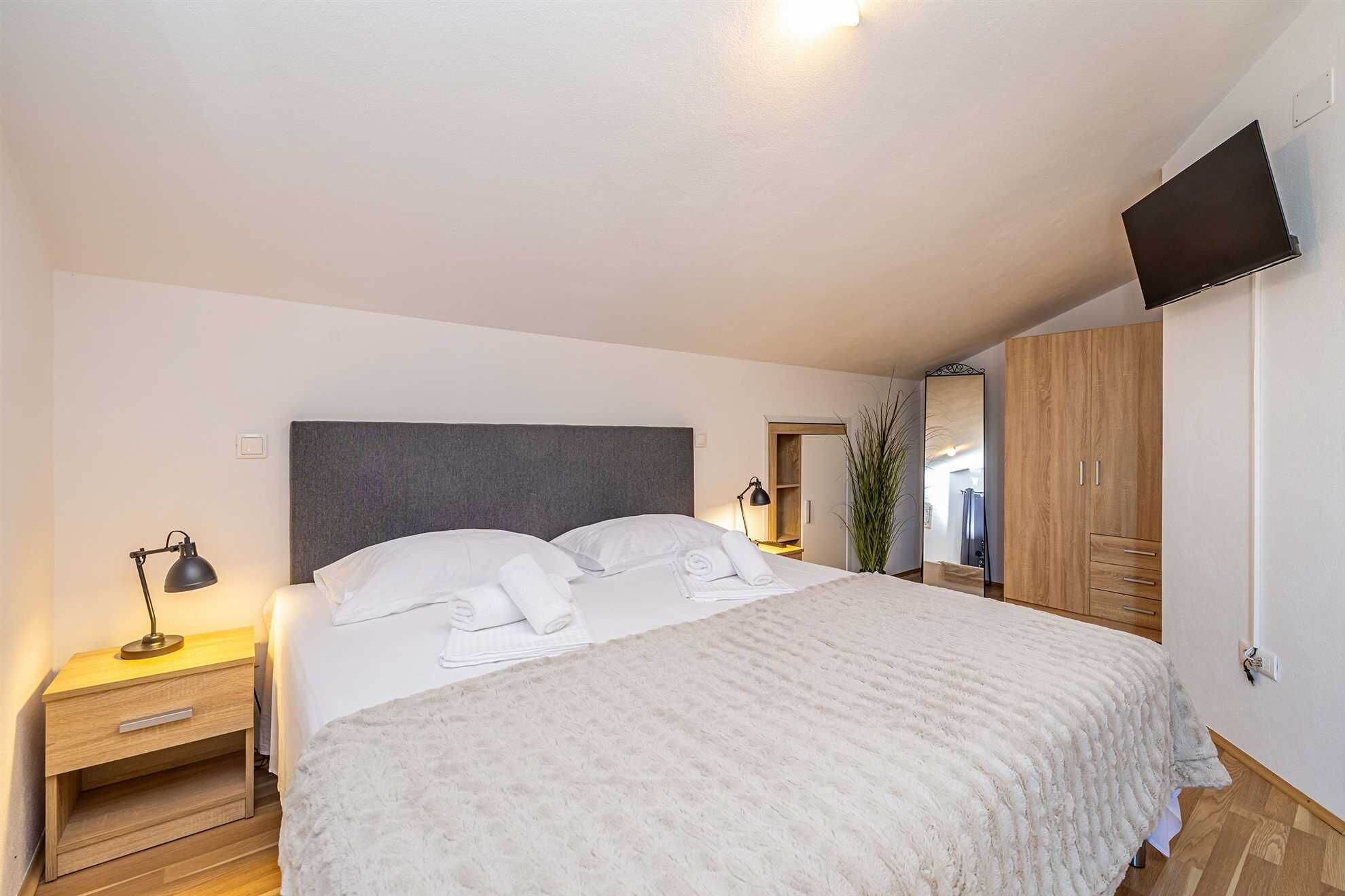 Une chambre à coucher comprenant un lit, une table de chevet, une lampe, une armoire et un téléviseur fixé au mur.