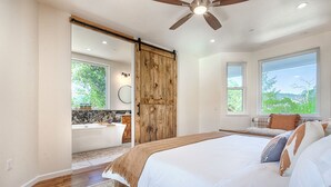 A bedroom with a large bed, a sliding barn door, a bathtub, and a view of greenery. - Modern Farmhouse with Pool & Vineyard (Santa Rosa)
