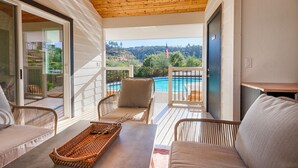 A covered outdoor area with wicker furniture, a table, and a view of a swimming pool and hills. - Modern Farmhouse with Pool & Vineyard (Santa Rosa)