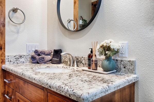 A bathroom with a granite countertop, a sink, a mirror, a towel rack, and a vase with flowers.
