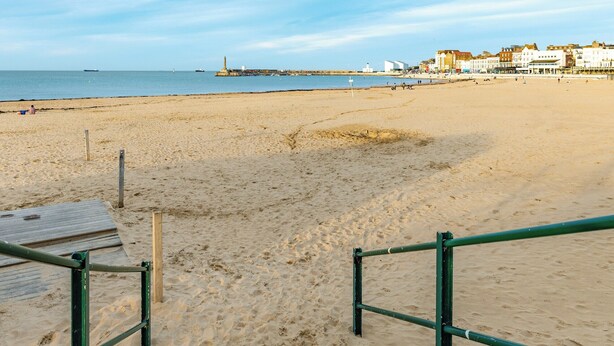 A sandy beach with a wooden structure and metal railings, a pier with buildings in the background, and a clear sky. - Beach Oasis Cottage - UK48530 (Margate)