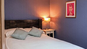 A neatly made bed with two patterned pillows, a bedside table with a lamp, and a framed artwork on the wall. - Beach Oasis Cottage - UK48530 (Margate)