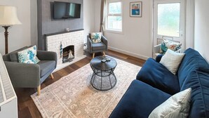A living room with a fireplace, a TV mounted on the wall, a sofa, a chair, and a coffee table. - Beach Oasis Cottage - UK48530 (Margate)