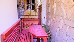 Un banc et une table rouges se trouvent devant un bâtiment, lequel est agrémenté d’une grille en métal décorative et d’un pot de fleurs.