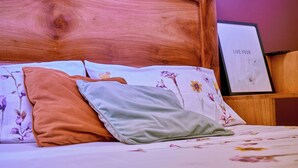 Un lit avec une literie à motifs floraux, une tête de lit en bois et une citation inspirante encadrée accrochée au mur.